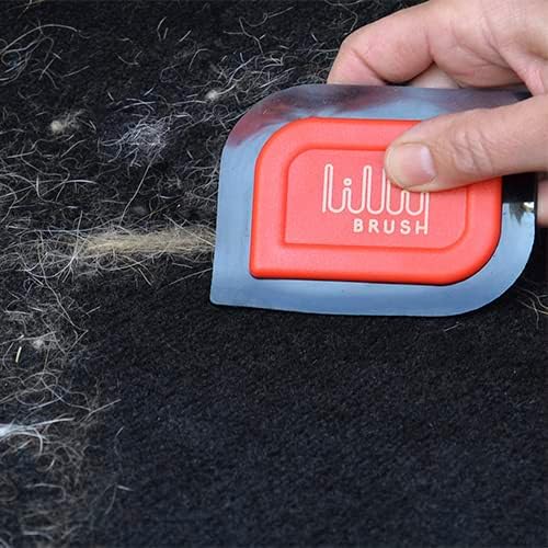 Hand using a red and blue pet grooming brush on dark fabric with loose fur.