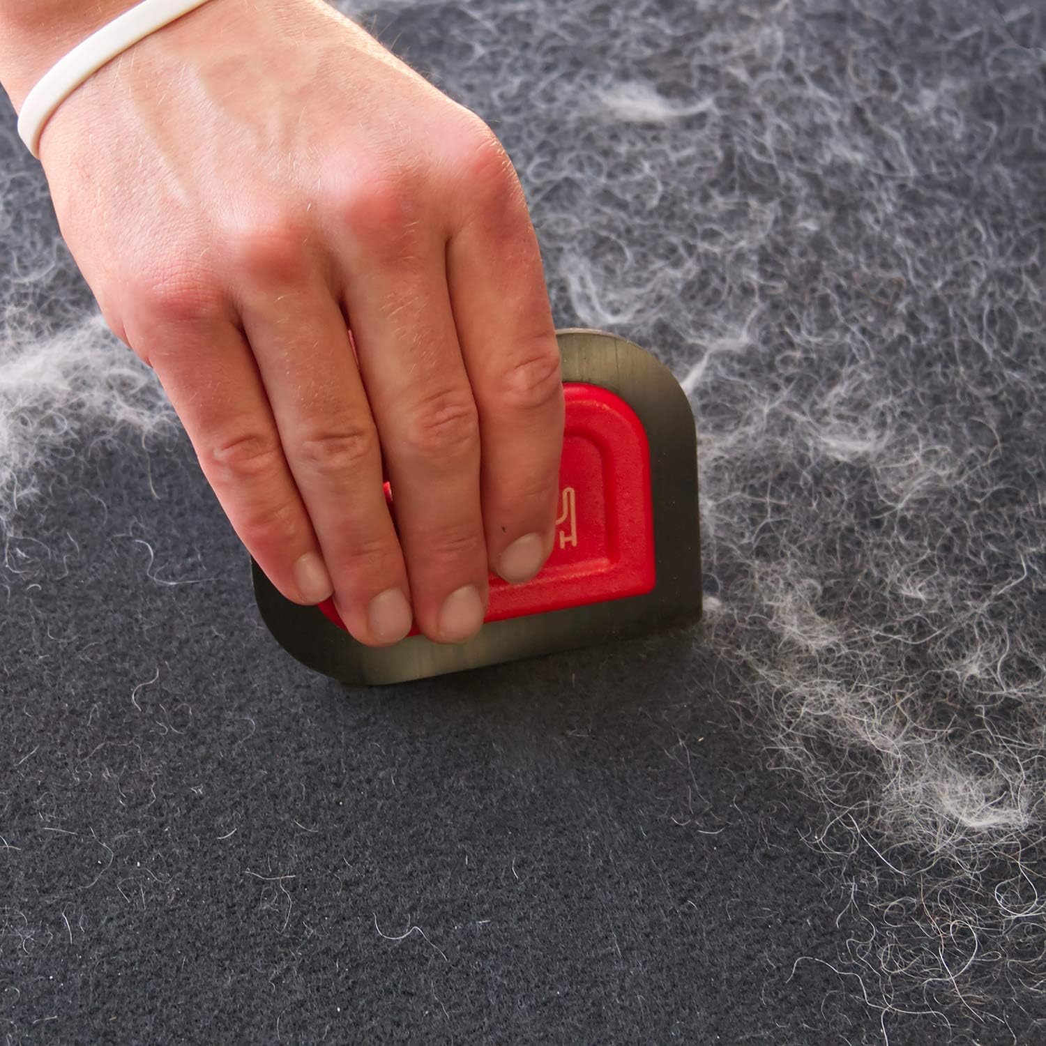 Hand using a pet hair removal tool on a surface with pet hair.