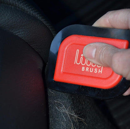 Person using a red and black car detailing brush on a car seat.